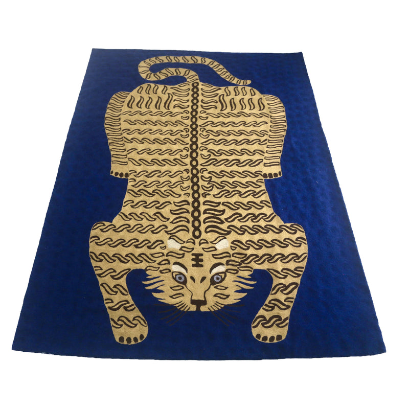 Bengal Tiger Carpet Royal Blue. Each carpet is made by hand by skilled artisans in Kashmir, the most northern part of India. Using a technique called chainstitch, colourful pure wool yarn is stitched by hook through cotton. Each carpet takes up to two months to complete.   We are stocking these beautiful carpets in a selection of bold colours in very small quantities. This one is a golden-beige tiger on a royal-blue background. 
